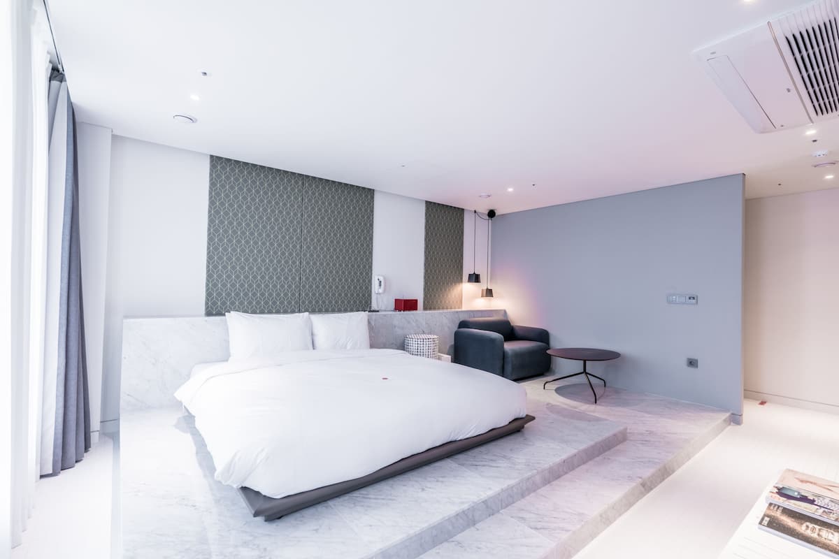 Una habitación de hotel moderna con una cama grande, un rincón de descanso con una mesita y un aire acondicionado instalado en la pared.