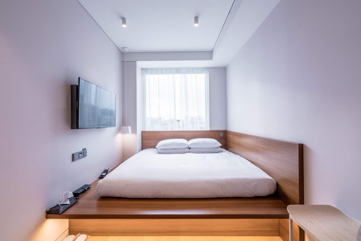 Un dormitorio moderno con una cama, un televisor montado en la pared y una ventana con cortinas de gasa.