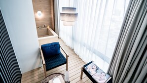 A modern hotel room with a wooden floor, a blue cushioned chair, a small table with a magazine, and a large window with sheer curtains. - Patio7 Hotel (Seoul)