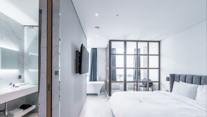 A modern hotel room with a large bed, a vanity with a mirror, a bathtub, and a television. - Patio7 Hotel (Seoul)