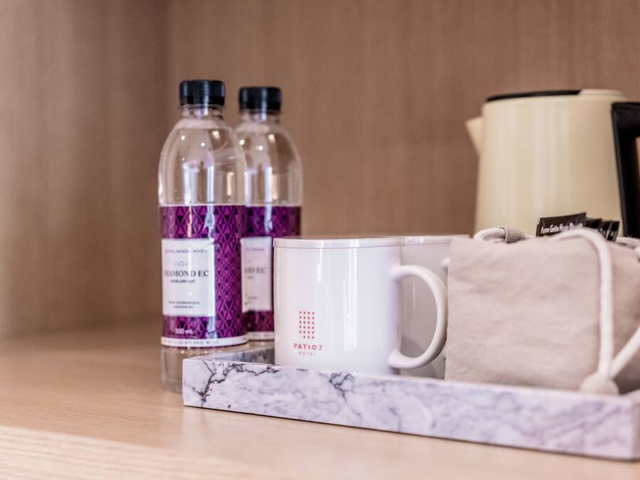Bandeja con taza blanca, dos botellas de agua, una bolsita de té y una tetera sobre superficie de madera.