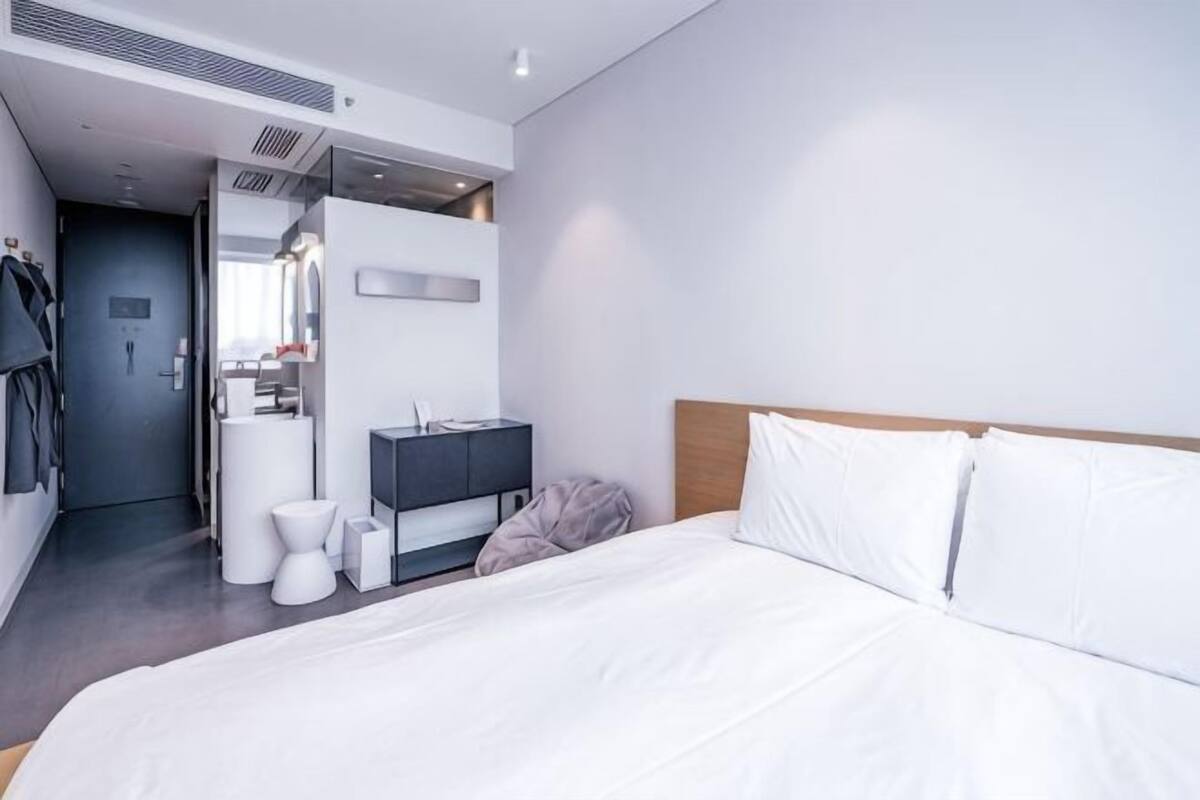 Una habitación de hotel moderna con una cama grande, una mesita de noche, un espejo, un armario y un baño con inodoro y lavabo.