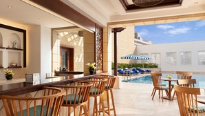 A poolside bar area with wooden chairs and a pool view. - Al Najada Doha Hotel by Tivoli (Doha)