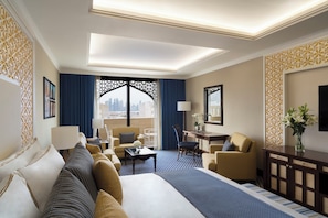 Habitación de hotel con una cama grande, un sofá, un escritorio y una silla. Se aprecia vista de la ciudad a través de las ventanas.
