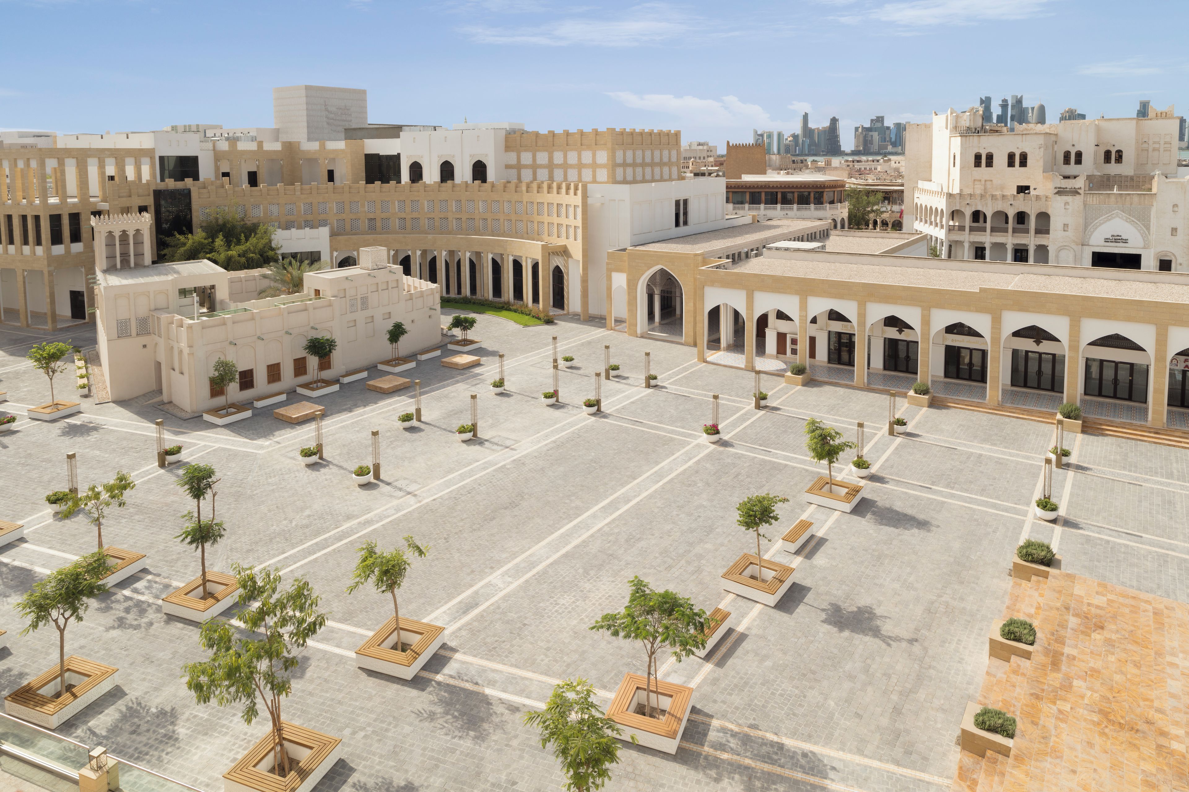 Un patio amplio con varios edificios, incluyendo una estructura blanca destacada con arcos y un espacio abierto con plantas en macetas.