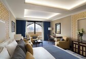 A hotel room with a large bed, a desk, a chair, a sofa, and a view of the city through a large window.