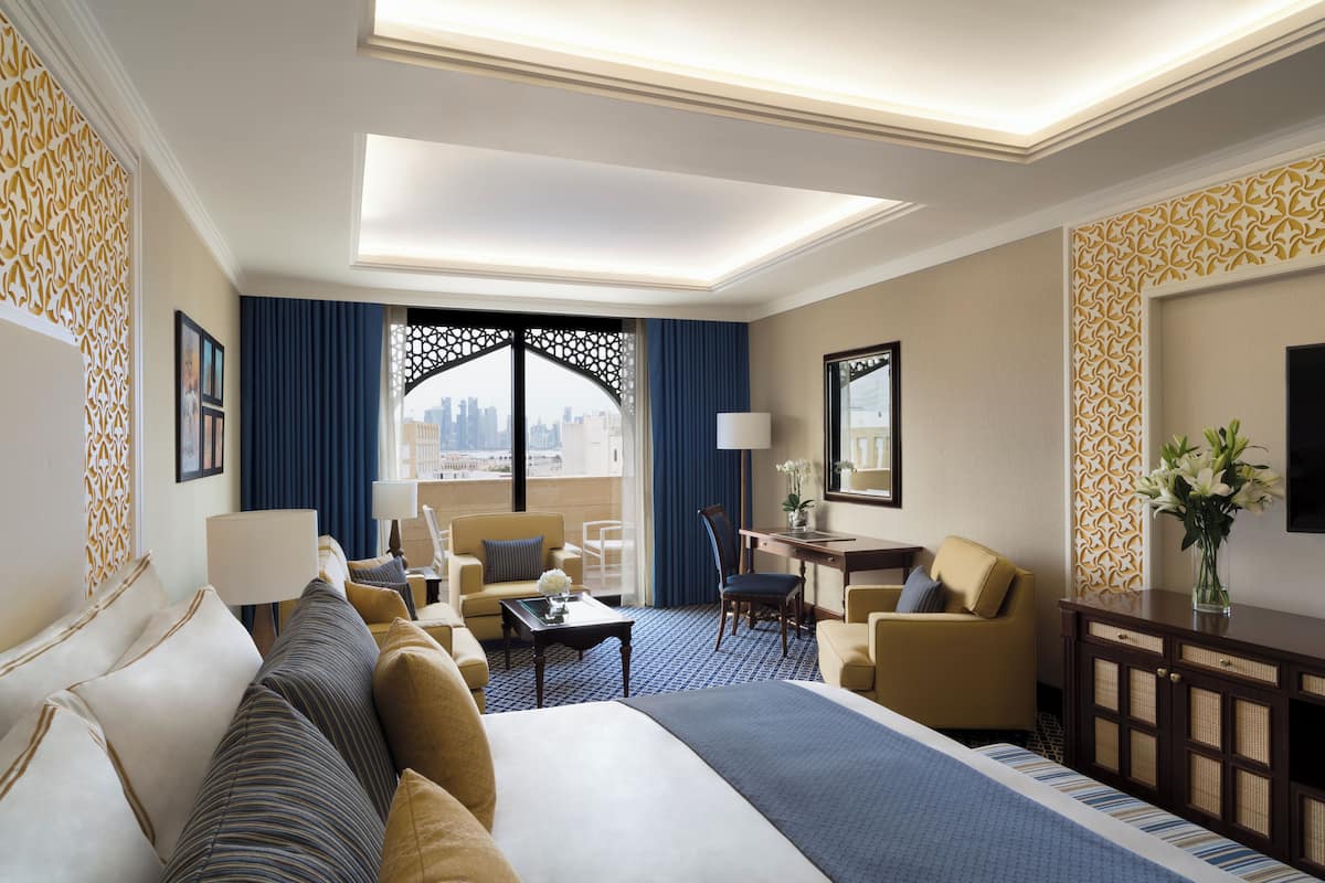 A hotel room with a large bed, a desk, a chair, a sofa, and a view of the city through a large window.