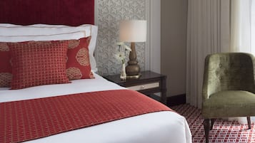 A hotel room with a large bed, a nightstand with a lamp, a green armchair, and patterned wallpaper.
