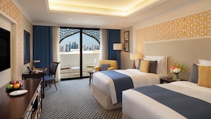 A hotel room with two beds, a desk, a chair, a TV, and a balcony with a city view. - Al Najada Doha Hotel by Tivoli (Doha)