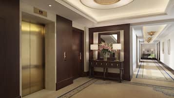 Un vestíbulo de hotel con un ascensor de madera, una consola con un jarrón de flores y un largo pasillo con cuadros enmarcados.