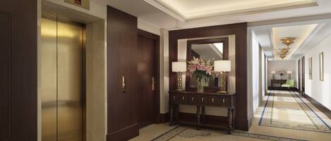 A hotel lobby with a wooden elevator, a console table with a vase of flowers, and a long corridor with framed pictures.