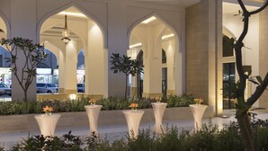 Ingresso di un hotel con colonne ad arco, illuminazione esterna e piante in vaso.
