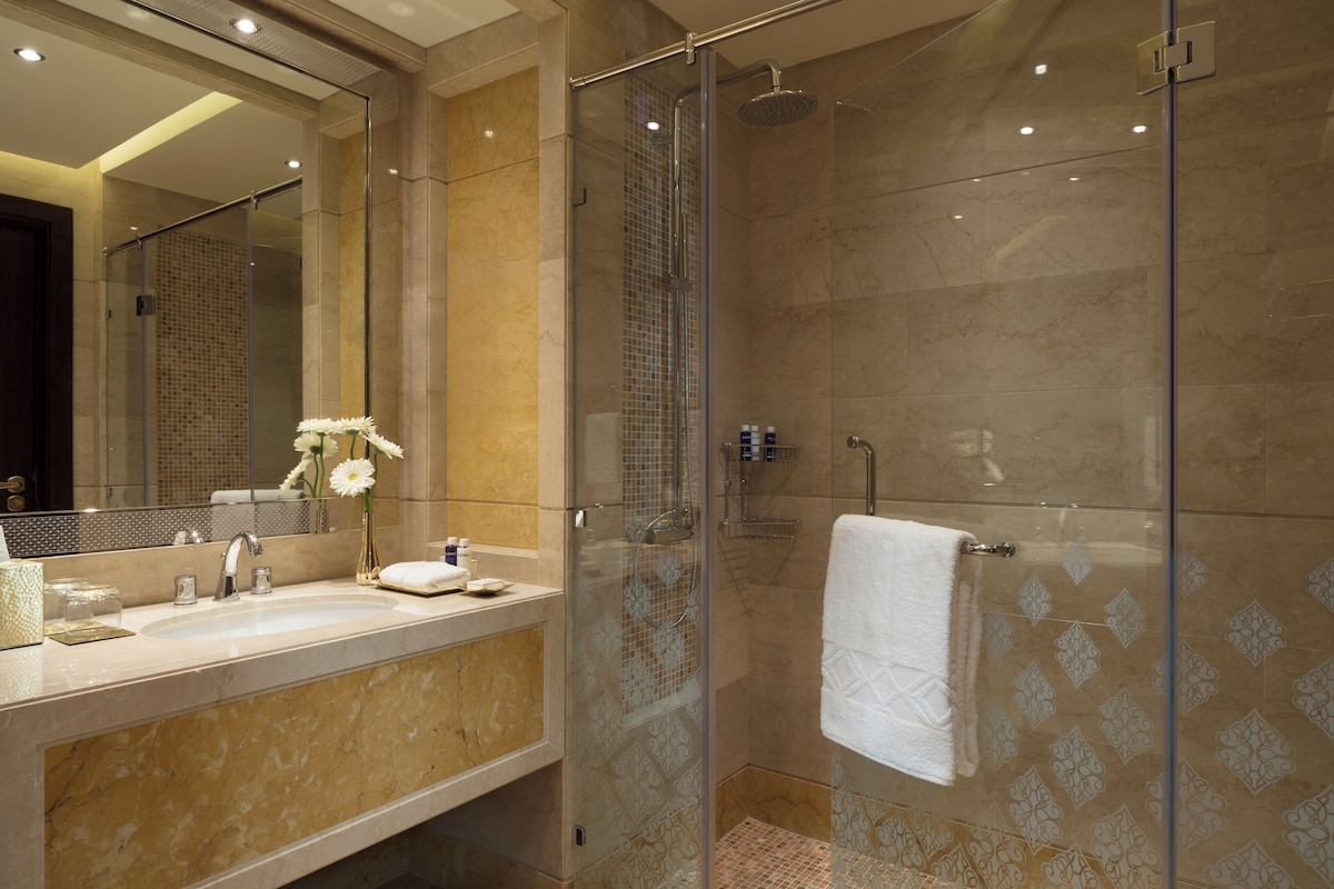 Un baño moderno con ducha envuelta en vidrio, lavamanos de mármol y un espejo grande.
