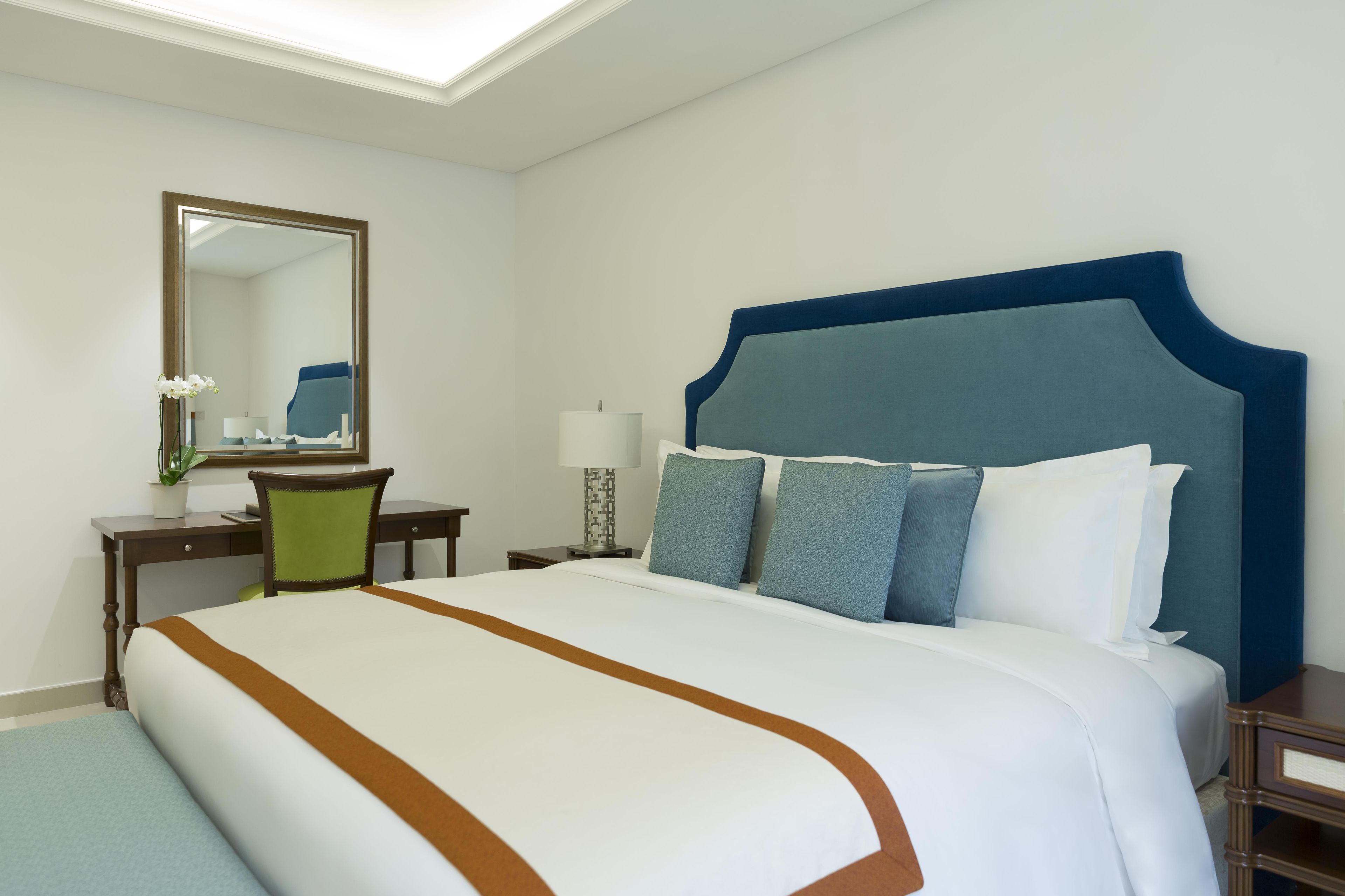 Habitación de hotel con una cama grande, un escritorio con una silla, una mesita de noche y un espejo en la pared.