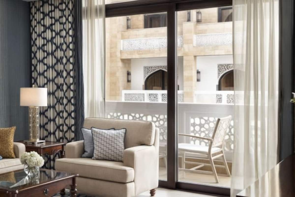 Una sala de estar moderna con un sofá, una mesa de centro y una lámpara. Hay un balcón con vistas a un edificio con balcones.