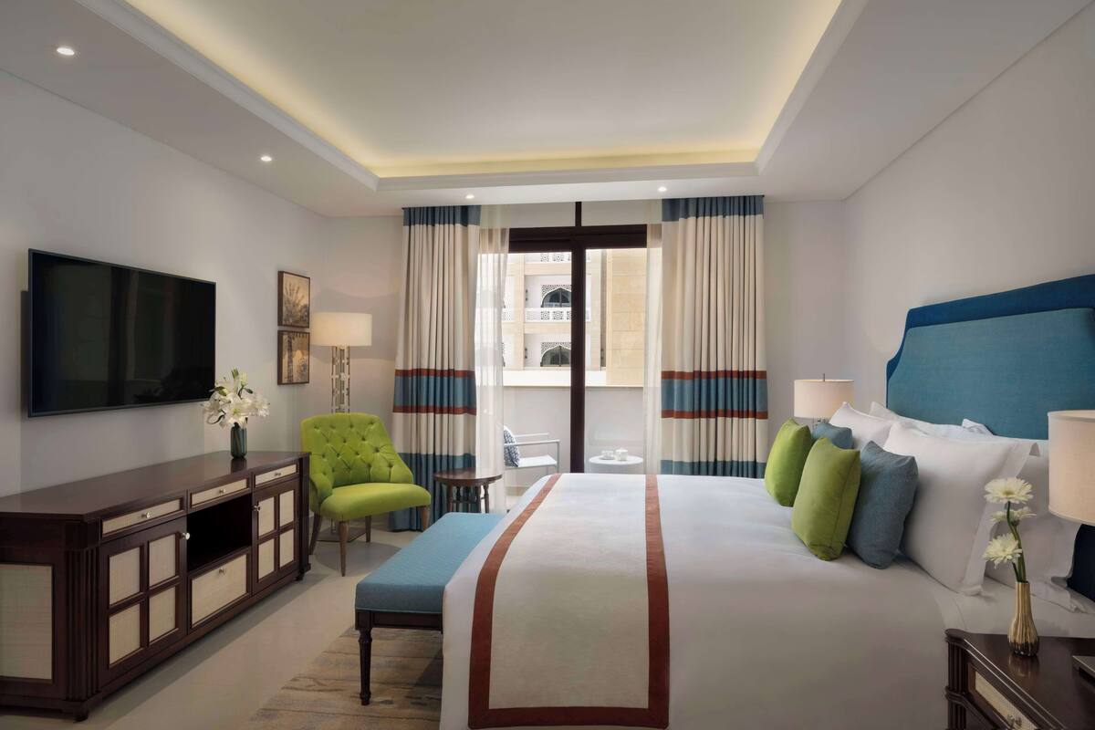 Een hotelkamer met een groot bed, een televisie, een groene fauteuil, een tafeltje en uitzicht op het balkon.