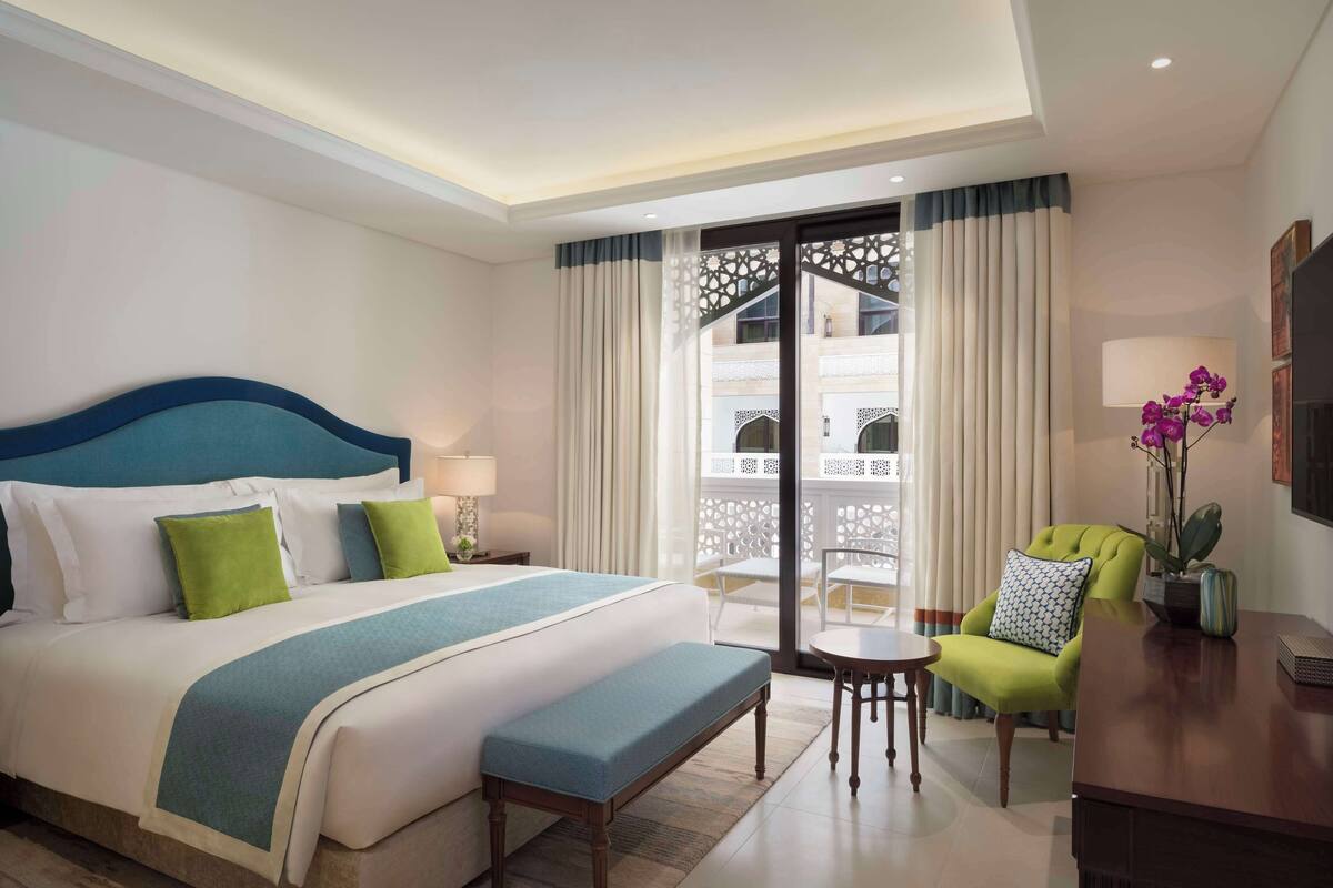 Hotelkamer met een groot bed, een bankje, een bureau, een stoel en een balkon met uitzicht.