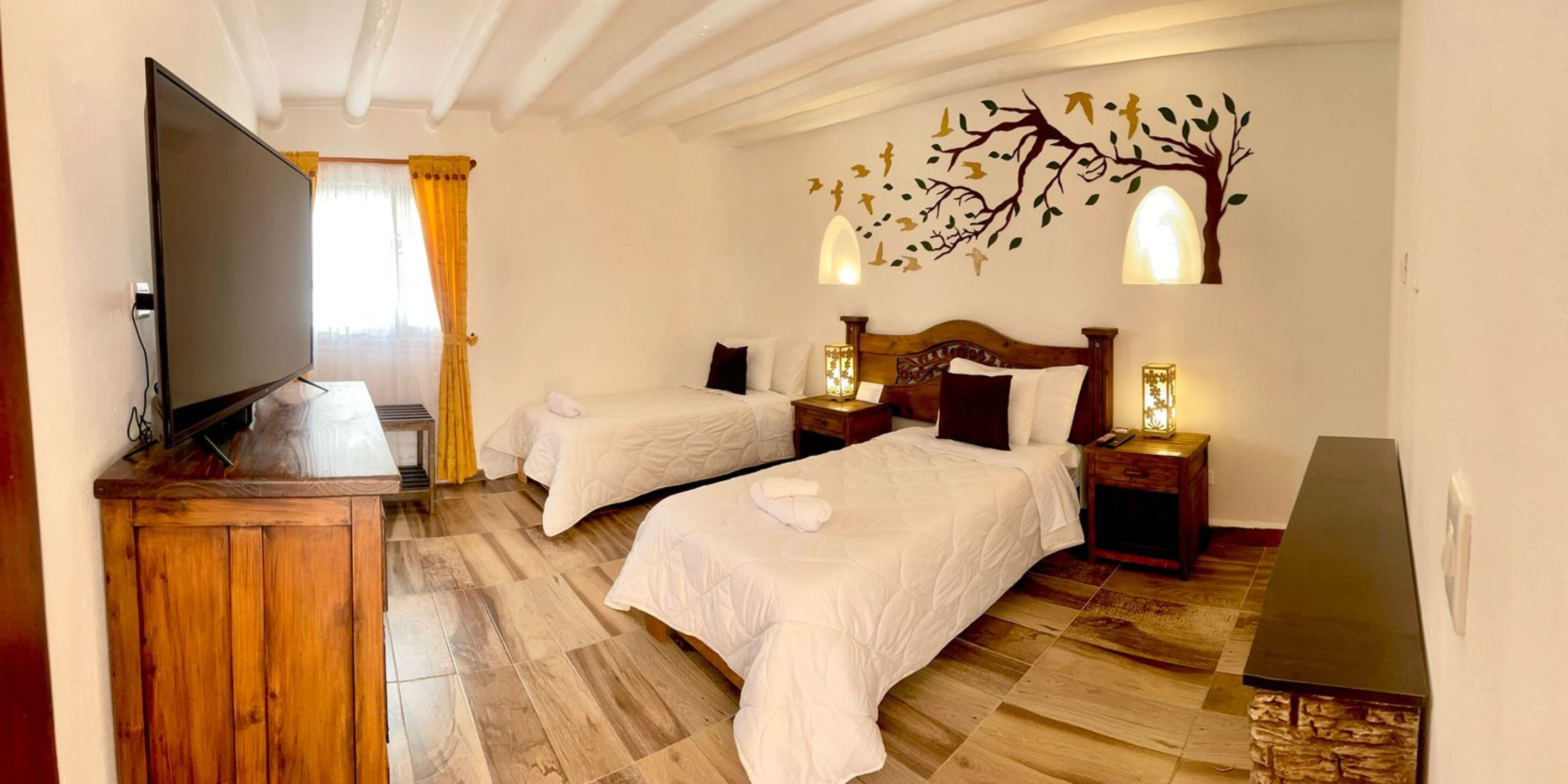 Habitación de hotel con dos camas, televisor, piso de madera y un mural decorativo.