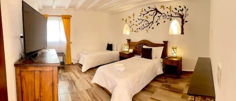 Habitación de hotel con dos camas, televisor, piso de madera y un mural decorativo.