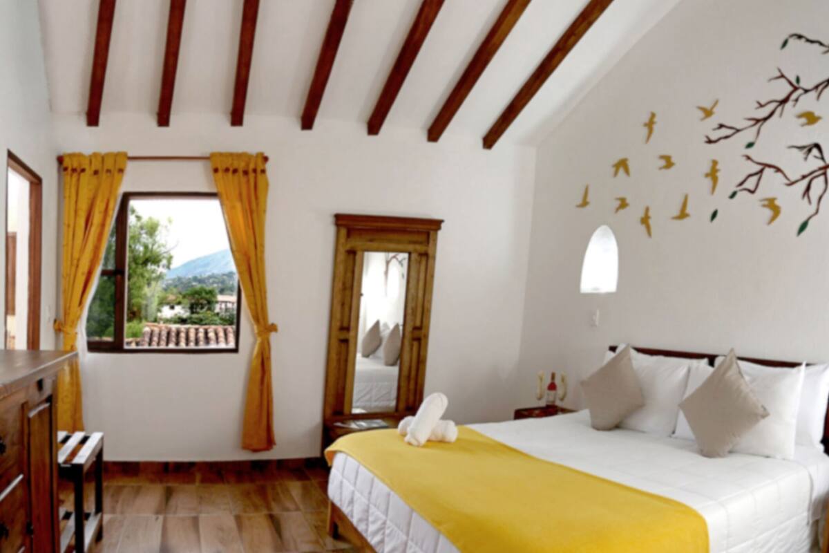 A hotel room with a bed, a TV, a window with curtains, and a view of the outdoors.