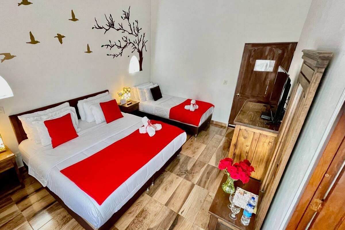 A hotel room with two beds, a wooden floor, a wall with bird decals, a tree decal, and a mirror cabinet.