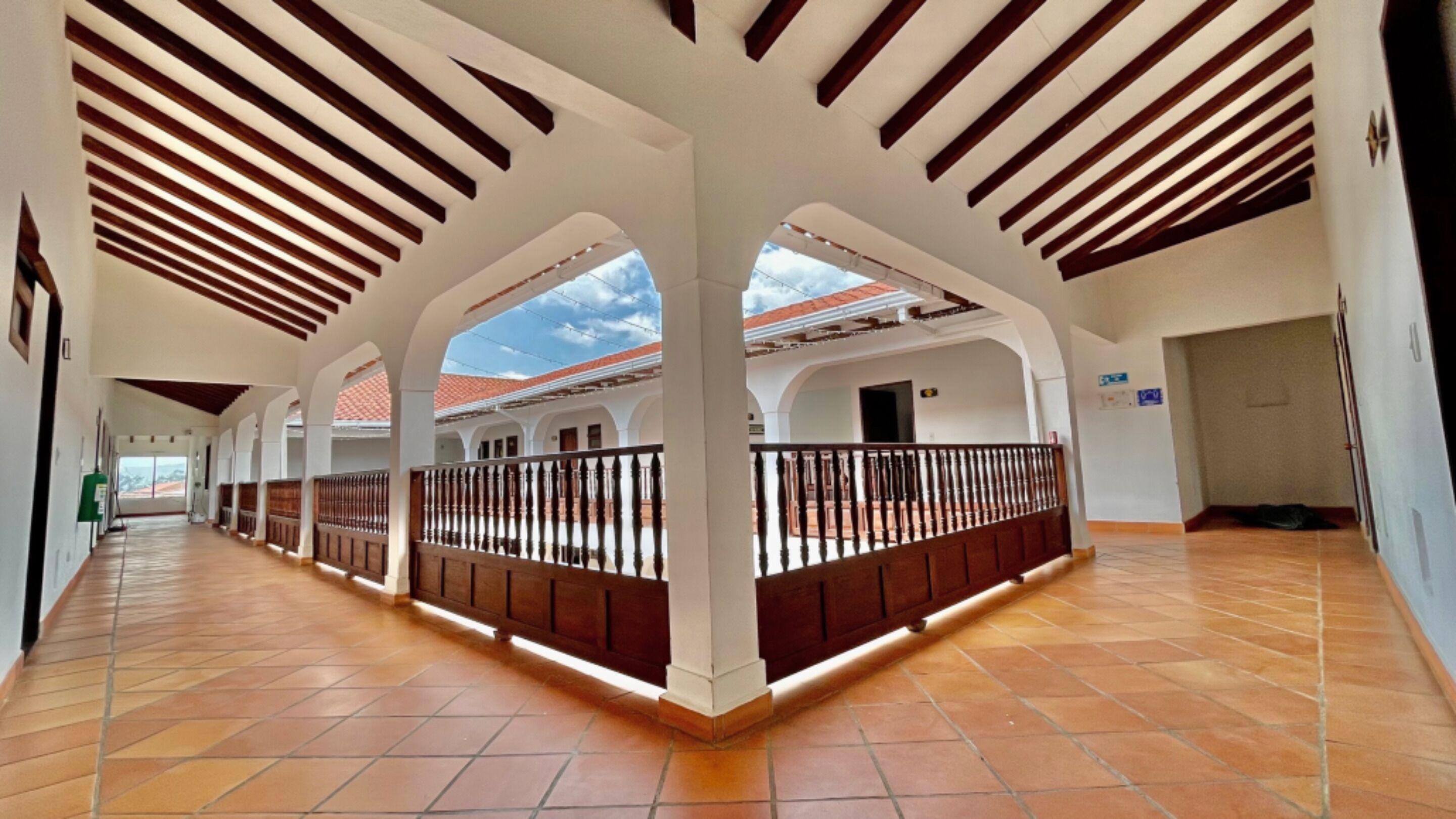 A spacious corridor with a tiled floor, white walls, and wooden beams on the ceiling.