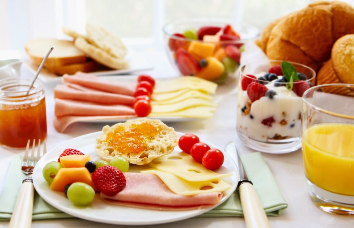 A breakfast table with various food items including eggs, cheese, ham, fruits, and pastries.