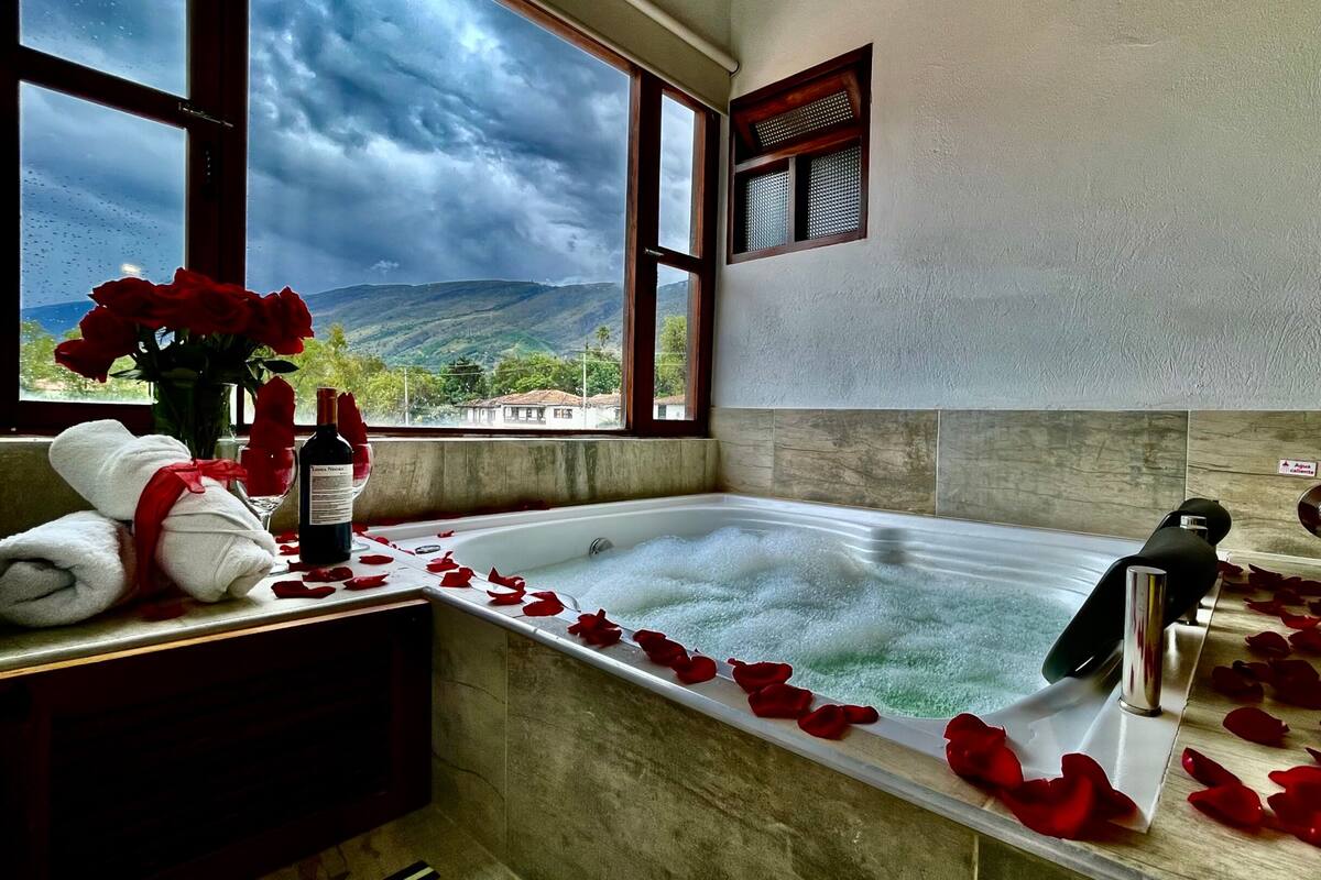 A bathroom with a bathtub, rose petals, towels, and a bottle of wine.