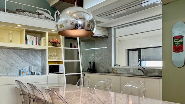 Una cocina moderna con encimera de mármol, una mesa de comedor con sillas transparentes y una lámpara colgante esférica original.