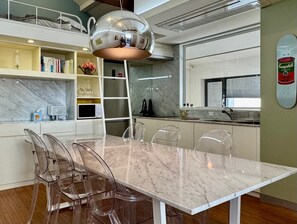 A modern kitchen with a marble countertop, a dining table with clear chairs, and a unique spherical pendant light.