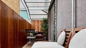 Un patio interior estrecho y cerrado con piso de madera, un sofá blanco y una mesa con sillas.