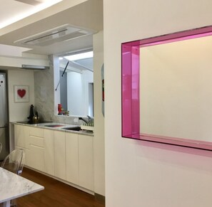 A modern kitchen with white cabinets, a marble countertop, and a pink-framed mirror.