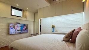 Un dormitorio con una cama grande, un televisor montado en la pared y un ventanal con cortinas.