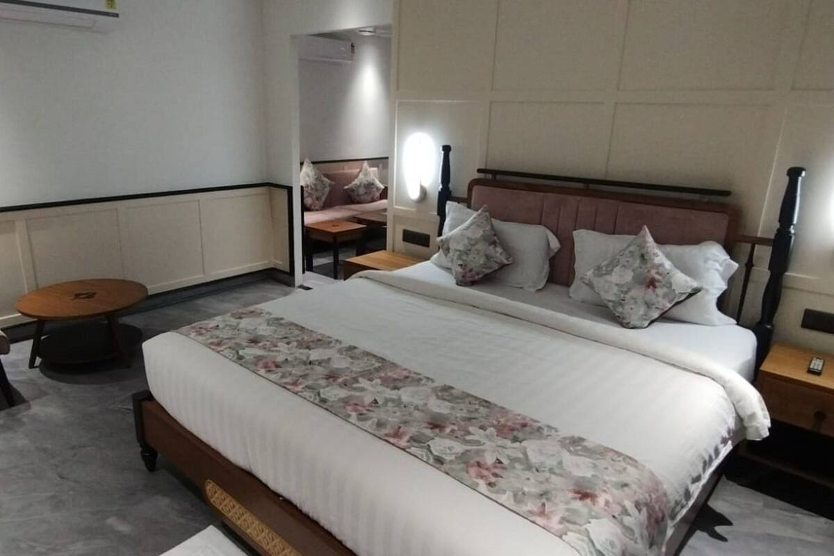A hotel room with a large bed, a small round table, a sofa, and a nightstand with a lamp.
