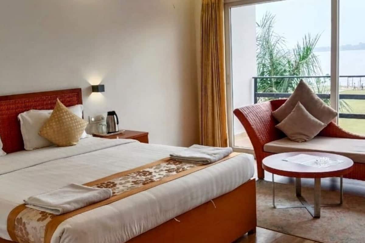 A hotel room with a large bed, a small table, a chair, and a view of the outdoors.