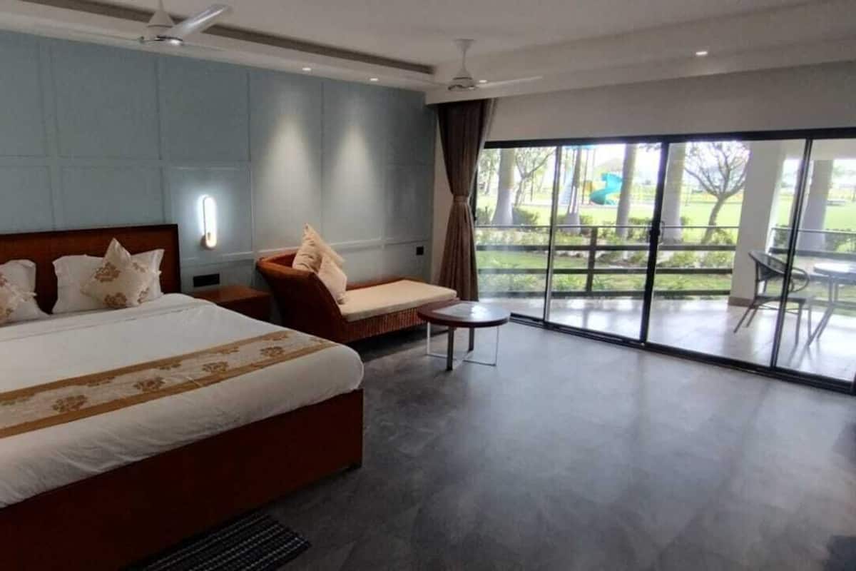 A modern hotel room with a large bed, a seating area with a chair and a small table, and a balcony with a view of the outdoors.
