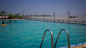 A swimming pool with clear blue water, metal pool ladders, and a view of the beach and ocean in the background.