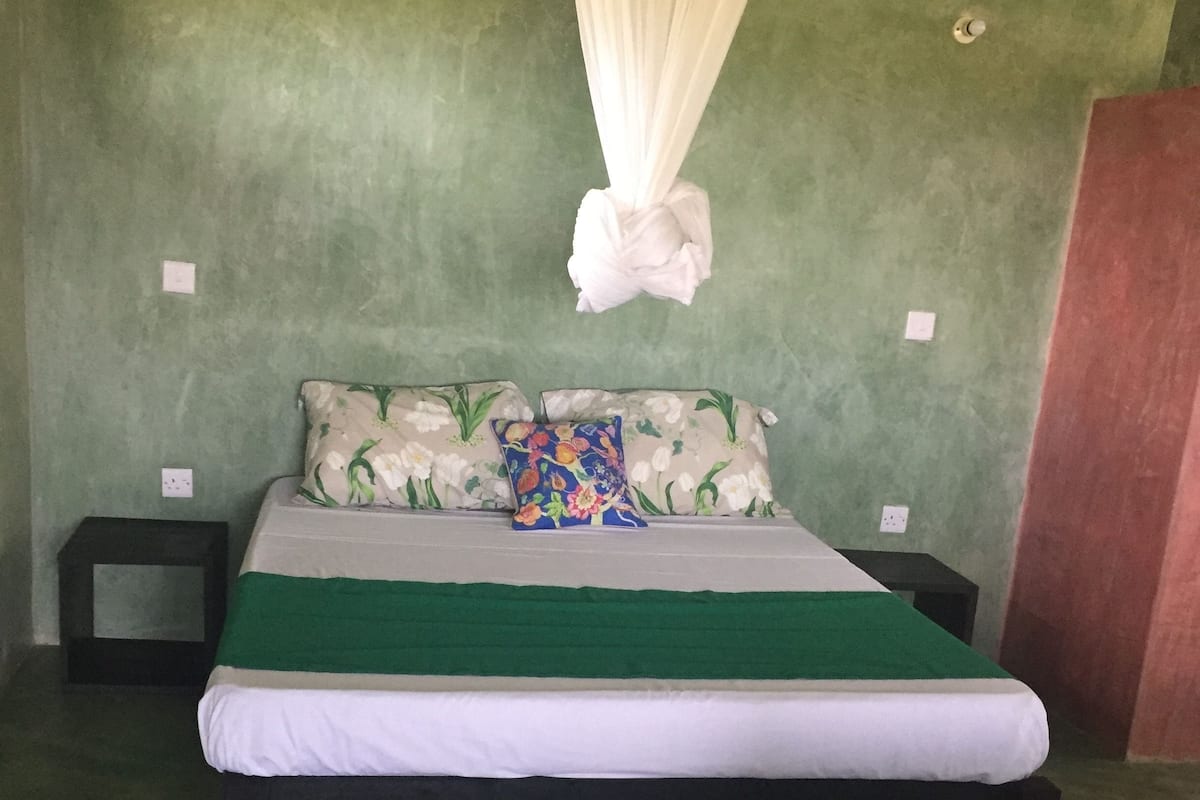 A bed with a green and white bedspread, floral pillows, and a white canopy.