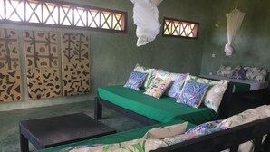 A room with a green sofa set, a wooden bench, and a small table. There are patterned cushions on the sofa. - Eagle Camp Mida Creek (Watamu)