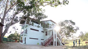 A two-story building with a staircase, surrounded by trees and a dirt ground. - Eagle Camp Mida Creek (Watamu)