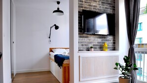 A modern bedroom with a bed, a mounted TV, a desk, and a potted plant. - Panda Apartments Grzybowska-Centrum (Warsaw)