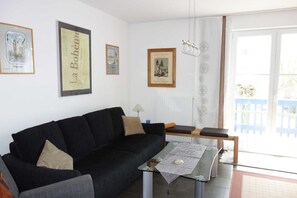 A living room with a black sofa, a glass coffee table, and framed pictures on the wall.