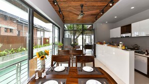 A modern kitchen with wooden ceiling, white cabinets, and a dining area with two tables set for four. - Sun Paradise Villa (Da Nang)