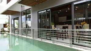 A modern indoor pool area with clear glass walls, a metal railing, and a view of the adjacent kitchen area. - Sun Paradise Villa (Da Nang)