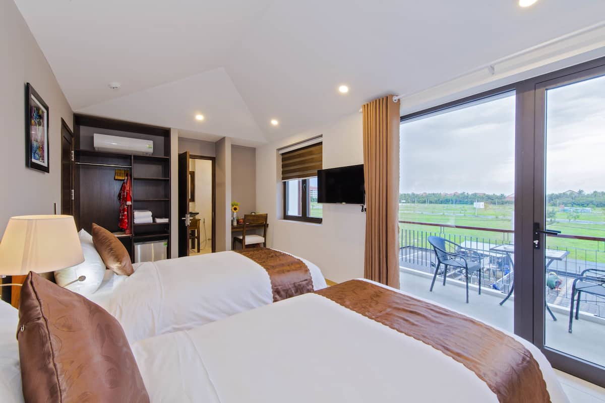 A hotel room with two beds, a TV, a balcony with outdoor seating, and a view of the countryside.