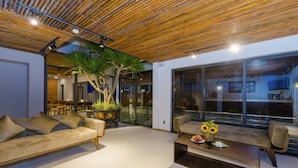 A modern living room with a wooden ceiling, a large window, and a potted plant. - Sun Paradise Villa (Da Nang)