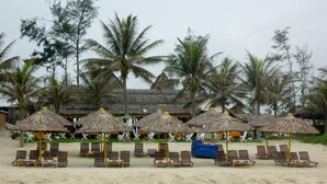 A beach with thatched umbrellas and wooden lounge chairs. - Sun Paradise Villa (Da Nang)