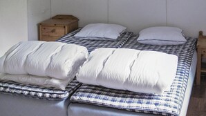 Una cama con una colcha a cuadros y almohadas blancas, una mesita de noche de madera y una lámpara de pared.