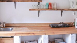 Una cocina con encimeras de madera, dos repisas colgantes con utensilios de cocina y una estufa de gas portátil.