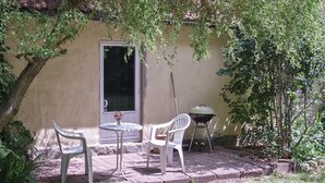 Un patio con dos sillas de plástico blancas, una mesa redonda pequeña y una parrilla.